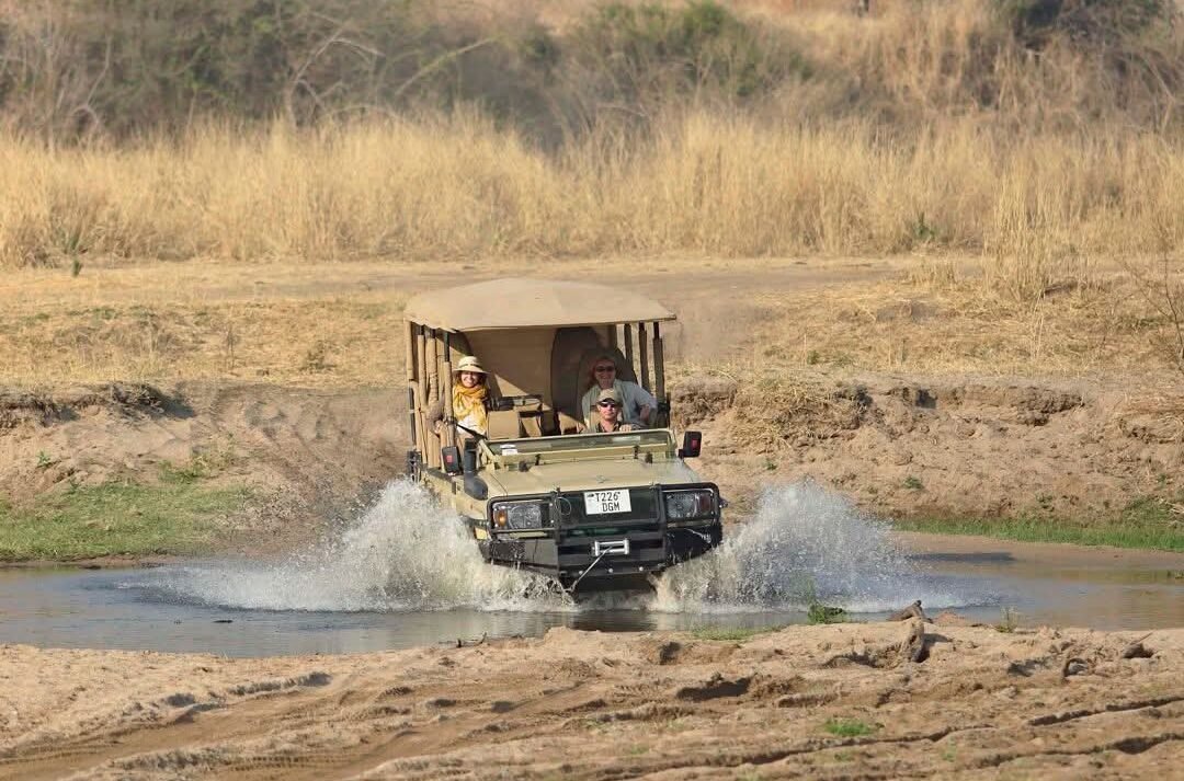 Safari vehicle crossing Mwagusi River during a morning game drive.